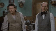 two men standing next to each other in a room with a green wall