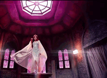 a woman in a white dress is standing on a pedestal in a room with pink windows .