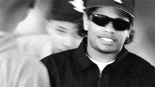a black and white photo of a man wearing a hat and sunglasses .
