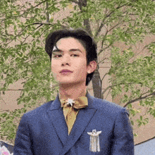 a young man wearing a suit and tie is standing in front of a tree .