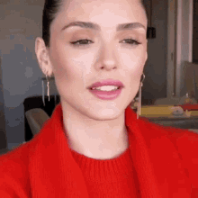 a woman wearing a red sweater and earrings is smiling .