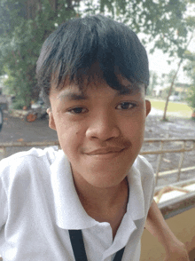 a young boy wearing a white polo shirt and black lanyard smiles for the camera