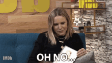 a woman sitting on a blue couch holding a piece of paper that says oh no on it