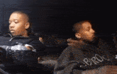 two men are sitting in a car and one of them is wearing a hoodie that says bro on it .
