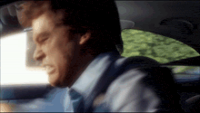 a man in a blue shirt and tie is driving a car with his eyes closed