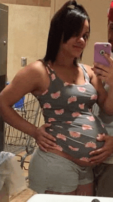a pregnant woman is taking a selfie in front of a mirror while holding her belly .