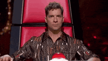 a man with curly hair is sitting in a red chair with a red button in front of him .