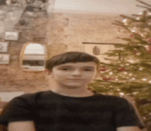 a boy in a black shirt is standing in front of a christmas tree .