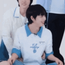 two young men are sitting next to each other on the floor and one of them is holding the other 's arm .