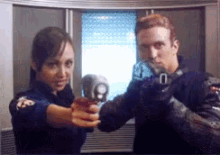 a man and a woman are pointing guns at each other in front of a window