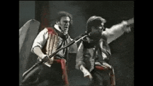 two men are standing next to each other on a stage holding swords and shields .