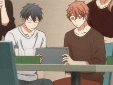 two anime characters are sitting at a table looking at a tablet computer