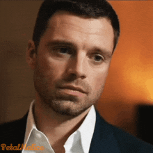 a man with a beard is wearing a suit and white shirt and looking at the camera .