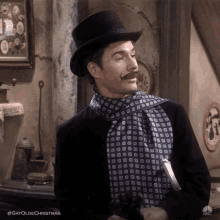 a man wearing a top hat and scarf is standing in a room .