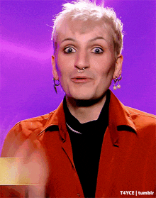 a man with a nose ring and earrings is wearing an orange shirt and black sweater