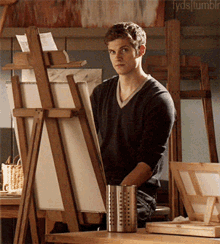 a young man is standing in front of an easel and looking at a canvas