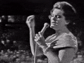 a woman singing into a microphone with a crowd behind her