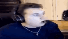 a man wearing headphones and a necklace with a cross on it is making a funny face .