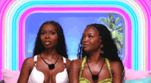 two women in bikinis are sitting next to each other on a bed .