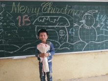 a young boy stands in front of a blackboard with merry christmas written on it
