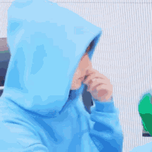 a young man wearing a blue hoodie is sitting in front of a white wall .