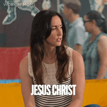 a woman is sitting on a yellow couch and the word jesus christ is on the screen behind her