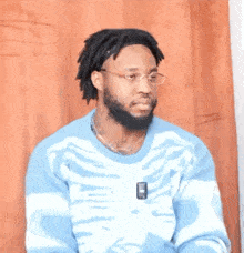 a man wearing glasses and a blue sweater with a skeleton on it is sitting in front of a curtain .