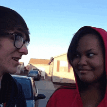 a man wearing glasses and a woman wearing a red hoodie are talking to each other