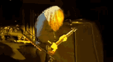 a man playing a guitar in a dark room with a yellow light behind him