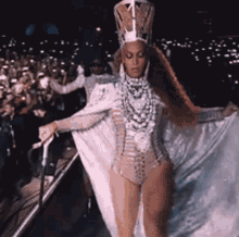 a woman wearing a crown and a bodysuit is standing on a stage in front of a crowd .