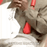a man in a suit and tie is holding a piece of paper in his hand and says `` genuine reaction '' .