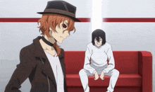 a man in a hat stands next to a man sitting on a red couch