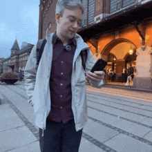 a man in a white jacket looks at his phone in front of a building