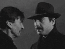two men are looking at each other and one is wearing a fedora