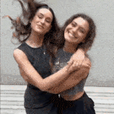 two women are hugging each other and smiling while their hair is blowing in the wind .