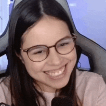 a woman wearing glasses is smiling in front of a microphone while sitting in a chair .