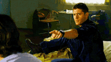 a man is sitting on a bed with his legs crossed and pointing at another man .