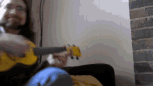 a man playing a yellow guitar in front of a white wall