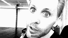 a black and white photo of a man with a beard making a funny face .