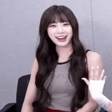 a woman with long hair is smiling and waving her hand .