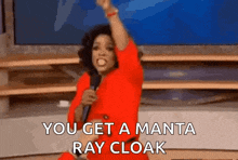 a woman in a red dress is holding a microphone and says `` you get a manta ray cloak ''