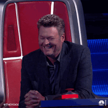 a man in a suit sits in a chair with a nbc logo on the bottom of it