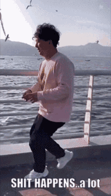 a man in a pink sweater is dancing in front of a body of water