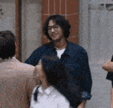 a man wearing glasses and a denim shirt is standing in a crowd of people .