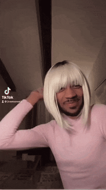 a man wearing a pink sweater and a blonde wig is making a funny face .