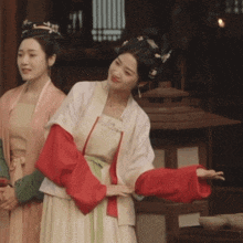 a woman in a white dress with red sleeves is standing next to another woman in a pink dress
