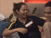 a woman wearing a kolette shirt is laughing while sitting on a couch