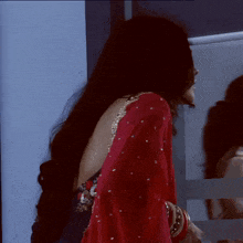 a woman in a red saree is standing in front of a white wall