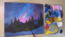 a painting of a night sky with trees and a palette of paint next to it