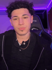 a man with curly hair is wearing a black jacket and a gold chain